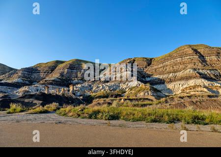 Einzigartige Sandsteinformationen, die als Hoodoos bekannt sind, ragen mitten in der erodierten Landschaft der Badlands empor, wobei sich auf dem Hügel deutliche geologische Schichten abzeichnen Stockfoto