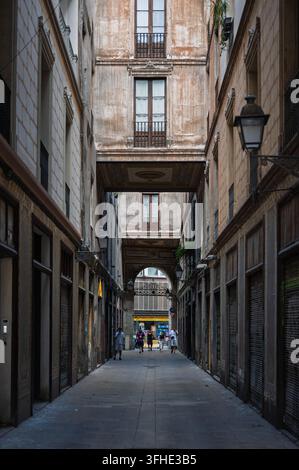Fußgänger gehen durch eine enge historische Gasse mit Bögen und traditionellen Balkonen in Barcelona, Spanien. Stockfoto