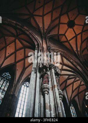 Schaut man direkt nach oben in eine gotische Kathedrale, treffen sich aufwändige steinerne Kreuzrippengewölbe über geschnitzten Statuen von Heiligen, während farbenfrohes Stained-Glass leuchtet Stockfoto