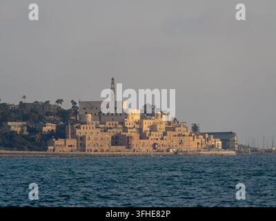 Die historischen Steinbauten und der Uhrturm von Alt-Jaffa erheben sich über der Küste, badend in warmem Licht der Goldenen Stunde, wie vom Mittelmeer aus gesehen Stockfoto