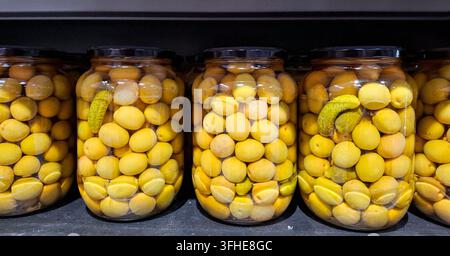 Eine Reihe durchsichtiger Gläser ist mit eingelegten grünen Oliven, Gurkchen und Knoblauch in Lake gefüllt. Dies zeigt traditionelle spanische Tapas und Hausgemachtes Stockfoto