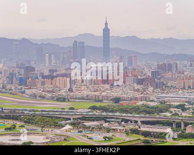 Taipei 101 erhebt sich über einer dichten städtischen Landschaft aus Hochhäusern und niedrigen Wohngebieten in der Nähe einer Flughafenlandebahn. Stockfoto