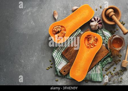 Rohe Kürbis Hälften oder butternut squash, Schneidbrett, Kräuter, Honig auf grauem Hintergrund. Ansicht von oben, flach, kopieren Raum Stockfoto