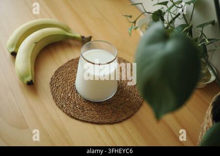 Milch in einem Glas, das auf einer Tischplatte platziert ist, mit Bananen daneben Stockfoto