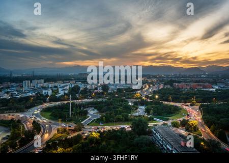 Sonnenuntergang an einer Kreisverkehrskreuzung während der abendlichen Hauptverkehrszeit in Changping, Peking, mit den Western Hills im Hintergrund Stockfoto