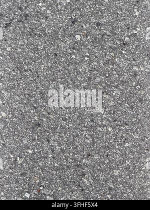 Detaillierte Nahaufnahme einer groben grauen Asphaltfläche mit sichtbarem Steinmaterial, das eine natürliche Straßenstruktur bildet. Stockfoto