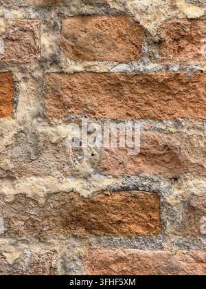 Nahaufnahme einer alten freigelegten roten Ziegelwand mit unregelmäßigem Mörtel, rissigem Putz und natürlich verwitterter Mauertextur. Stockfoto