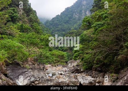 Sanzhanxi-Flusstal in Hualien, Taiwan. Felsenreiches Flussbett, das in üppige grüne Berge mündet. Dichte tropische Waldbedeckung. Stockfoto