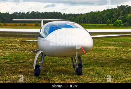 Weißes Gleitflugzeug steht auf einem grünen Grasflugplatz, mit einer sichtbar in der Hintergrund gegen einen bewölkten Himmel liegenden Landebahn Stockfoto