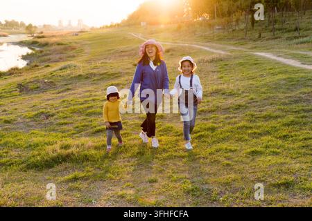 Mutter und Töchter laufen und halten sich an der Hand auf einer Wiese bei Sonnenuntergang Stockfoto