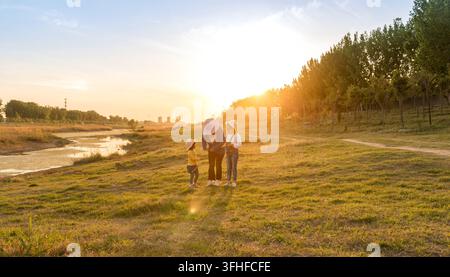 Mutter und Töchter laufen und halten sich an der Hand auf einer Wiese bei Sonnenuntergang Stockfoto