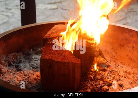 Helle orangefarbene Flammen und Funken steigen von brennenden Holzscheiten in einer großen metallenen Ritualfeuerstelle im August 2026 auf. Stockfoto