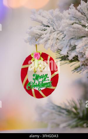 Weihnachtsbaumschmuck mit dem Text Frohe Weihnachten, der an einem schneebedeckten Zweig hängt Stockfoto