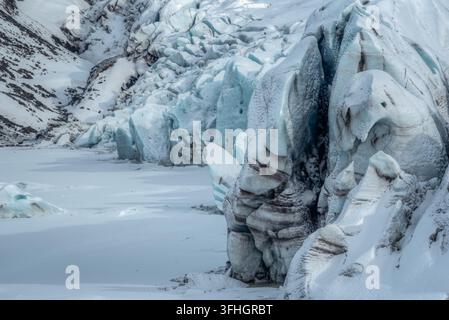 Blick auf einen massiven Gletscher mit gezackten blauen Eisformationen und tiefen Spalten vor der Kulisse einer schneebedeckten Berglandschaft in Island. Stockfoto