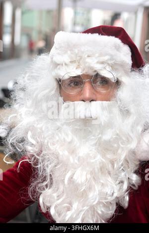 Nahaufnahme-Porträt von Santa Claus in traditioneller roter Kleidung, weißem Bart und runder Brille, während er direkt in die Kamera schaut. Stockfoto