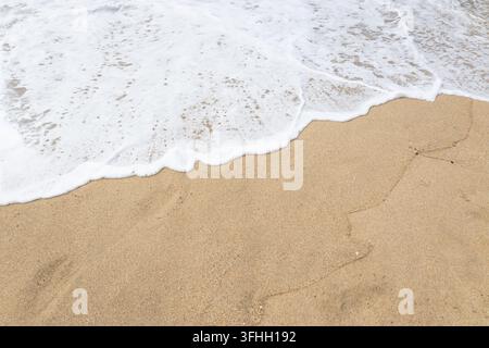 Schaum einer Meereswelle auf goldenem Sandstrand als Hintergrund Stockfoto