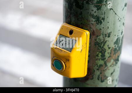 Vordergrund eines gelben Fußgänger-Druckknopfes, der an einem alten verwitterten grünen Signalpfosten montiert ist, mit einer Handikone und einem grünen Aktivierungsknopf für s Stockfoto