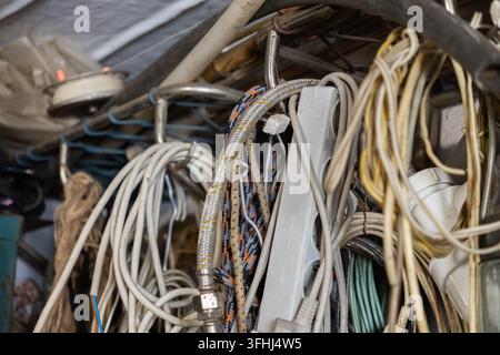 Unorganisierter Haufen von hängenden Kabeln, Steckdosenleisten und geflochtenen Schläuchen, die an Metallhaken gelagert sind und eine rohe visuelle Darstellung von industrieller Unordnung bieten Stockfoto