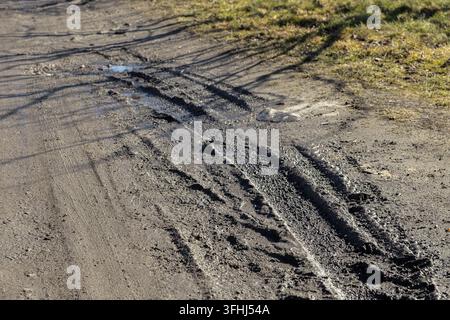 Muddyter Pfad, markiert durch deutliche Reifenspuren und kleine Pfützen, die die schwierigen Bedingungen auf beschädigten Landstraßen darstellen Stockfoto