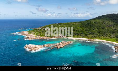 Felsige Küste mit türkisfarbenem Ozeanwasser unter einem klaren Himmel. La Digue, Seychellen. Stockfoto
