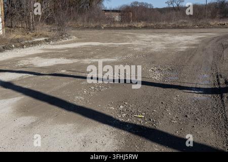 Eine verlassene, raue Piste aus Schotter und Erde führt durch eine karge Landschaft unter einem hellen Himmel und vermittelt Themen der Isolation, Vernachlässigung und De Stockfoto