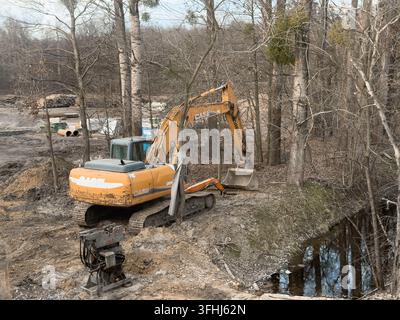 Wroclaw, Polen - 8. März 2026: Ein Kastenbagger ruht neben einem kleinen Bach auf einer Waldlichtung und veranschaulicht schwere Maschinen, die für Land genutzt werden Stockfoto