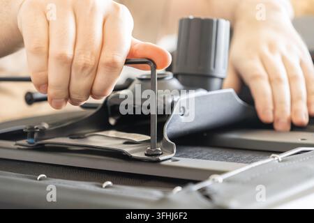 Nahaufnahme von Händen, die einen Bürostuhl montieren, indem sie Schrauben mit einem Inbusschlüssel befestigen, was den Prozess der Herstellung von Arbeitsplatzequipment, Selbstmontage, vermittelt Stockfoto