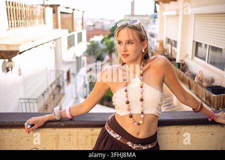 Junge Frau entspannt sich auf einer Dachterrasse, umarmt einen entspannten Sommerstil. Sie beobachtet die Stadt und die umliegenden Gebäude Stockfoto