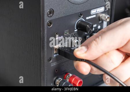 Hand, die einen Stecker in einen digitalen Audioeingang auf der Rückseite eines Studiolautsprechers steckt, zeigt den technischen Prozess der Installation von Heimunterhaltung Stockfoto