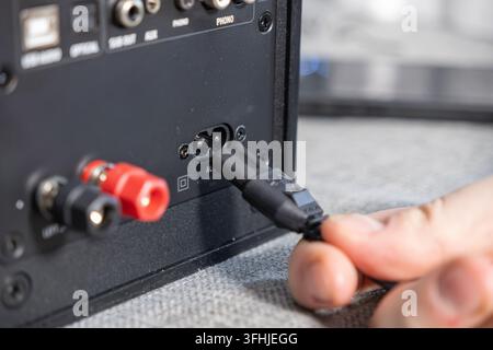 Person, die ein schwarzes elektrisches Kabel in die Rückseite eines Lautsystems steckt, veranschaulicht die Hardware-Installation und Konnektivität für Heimaudio Stockfoto