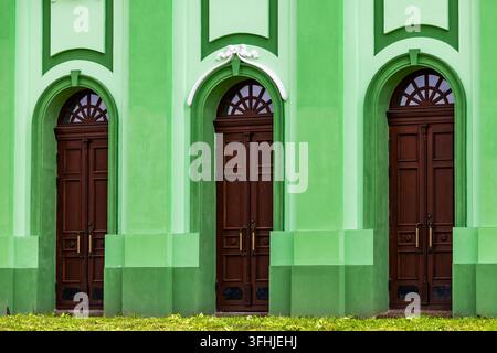 Drei hohe hölzerne Torbögen mit Oberlichtern reihen sich entlang einer lebhaft grün gestrichenen Gebäudefassade. Das symmetrische architektonische Design zeigt Stockfoto