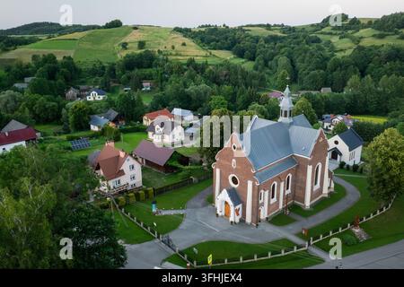 Luftbild des Dorfes Łubno in Podkarpackie, Polen, mit einer Kirche, die rechts zwischen Häusern und grüner ländlicher Landschaft sichtbar ist. Stockfoto