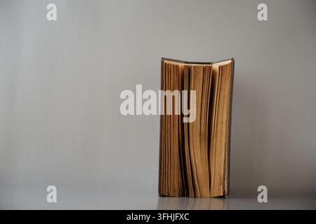 Ein altes halbgeöffnetes Buch steht auf einem grauen Hintergrund. Stockfoto