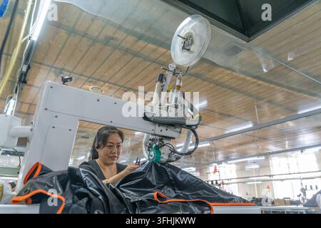 Luannan County, China – 30. Juli 2026: Frauen in einer Werkstatt nähen schwarze wasserdichte Planen mit Thermonähmaschinen Stockfoto