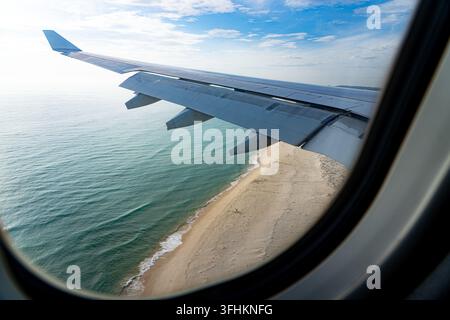 Ein malerischer Blick auf den Ozean und den Strand, aufgenommen vom Fenster eines Flugzeugs während des Fluges, der die Schönheit der Küstenlandschaften hervorhebt. Stockfoto