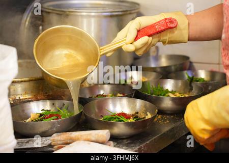 Heißes Brühe in Nudelschüsseln in einer koreanischen Restaurantküche gießen Stockfoto