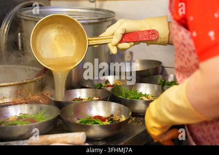 Heißes Brühe in Nudelschüsseln in einer koreanischen Restaurantküche gießen Stockfoto