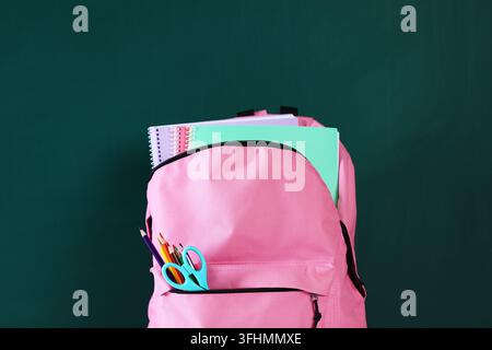 Rucksack mit Notizbüchern und Schreibwaren vor Kreidetafel, Nahaufnahme Stockfoto