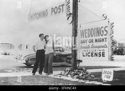 Ein Paar steht vor einer Hochzeitskapelle in Las Vegas, 1941, mit Schildern, die Tag und Nacht durchgeführte Ehen bewerben. Stockfoto