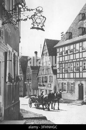 Ein pferdegezogener Karren mit zwei gespannten Pferden steht im Vordergrund einer schmalen Kopfsteinpflasterstraße in einer nicht identifizierten Stadt in Mittelfranken, 1944, mit Fachwerkhäusern und einem dekorativen Metallschild mit einem sechszackigen Stern. Stockfoto