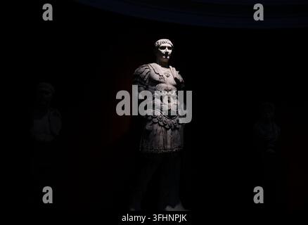 Marmorstatuie eines römischen Kaisers in prunkvoller Rüstung taucht aus tiefer Dunkelheit in einer schummrigen Halle der Ny Carlsberg Glyptotek auf Stockfoto