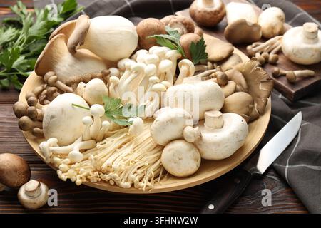 Viele verschiedene Pilze, Petersilie und Messer auf Holztablett, Nahaufnahme Stockfoto