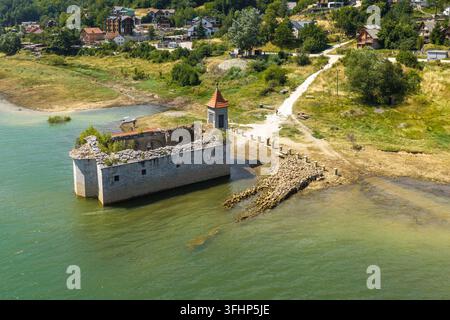 Luftbild der versunkenen Kirche St. Nikolaus, teilweise im Mavrovo-See versunken, mit Steinmauern, einem rot gedeckten Dach und der umgebenden grünen Landschaft Stockfoto