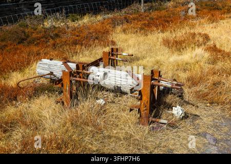 Gebrochener hölzerner Strommast, der in trockenem Gras im Dinorwic Schieferbruch in Llanberis, Wales, ruht, verrostete Eisenbeschläge und Keramikisolatoren sichtbar Stockfoto