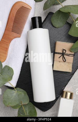 Flasche Shampoo, andere Kosmetikprodukte, Handtuch, Kamm und Eukalyptuszweige auf grauem Tisch, Flat Lay Stockfoto