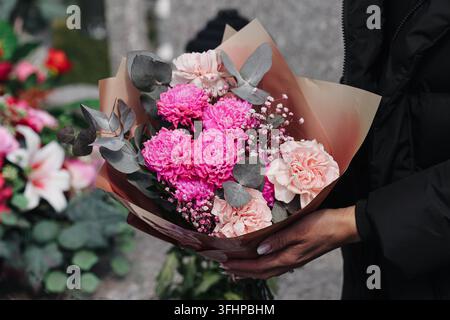 Person hält farbenfrohen Blumenstrauß, der in dekorativem Papier eingewickelt ist. Floraler Hintergrund für Geschenkfeier, Blumen, romantische Begrüßung und besondere Anlässe Stockfoto