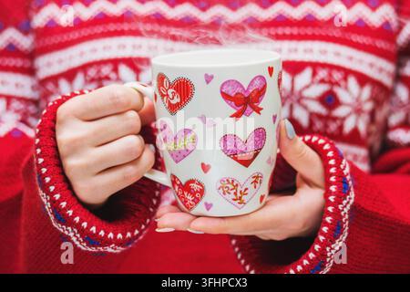 Frau in rot pullover hält einen Winter Cup mit Herzen. Winter und Weihnachten Konzept. Stockfoto
