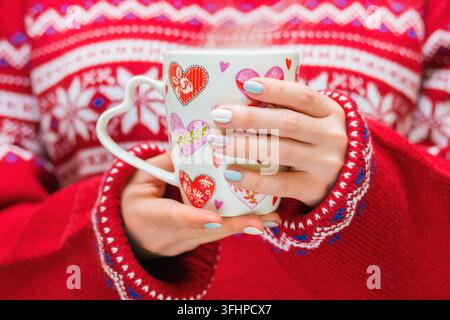 Frau in rot pullover hält einen Winter Cup mit Herzen. Winter und Weihnachten Konzept. Stockfoto