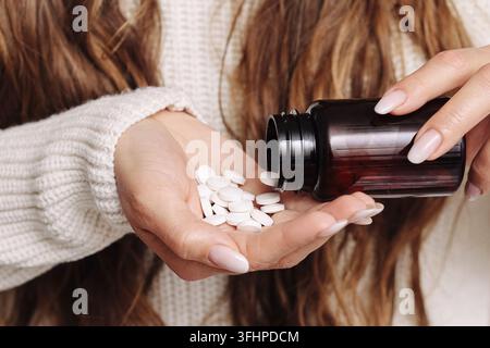 Frau gießt weiße Medizintabletten aus einer dunklen Flasche in die Hand. Gesundheitsversorgungs-Hintergrund für Medikation, Dosierung, Apotheke und tägliche medizinische Behandlung. Stockfoto