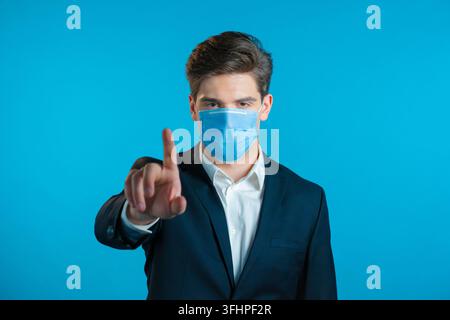 Porträt eines ernsten Geschäftsmannes in Berufskleidung und medizinischer Maske, der eine ablehnende Geste durch das Stoppzeichen mit dem Finger zeigt. Mann isoliert Stockfoto